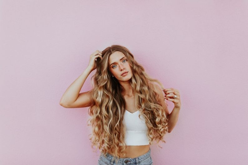 Balayage - woman standing next to pink wall while scratching her head