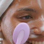 Skincare Routine - A woman is smiling while using a brush to clean her face