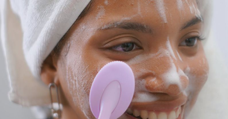 Skincare Routine - A woman is smiling while using a brush to clean her face