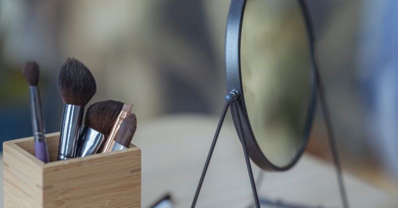 Foundation Application - Cosmetic brushes and round mirror placed on wooden table