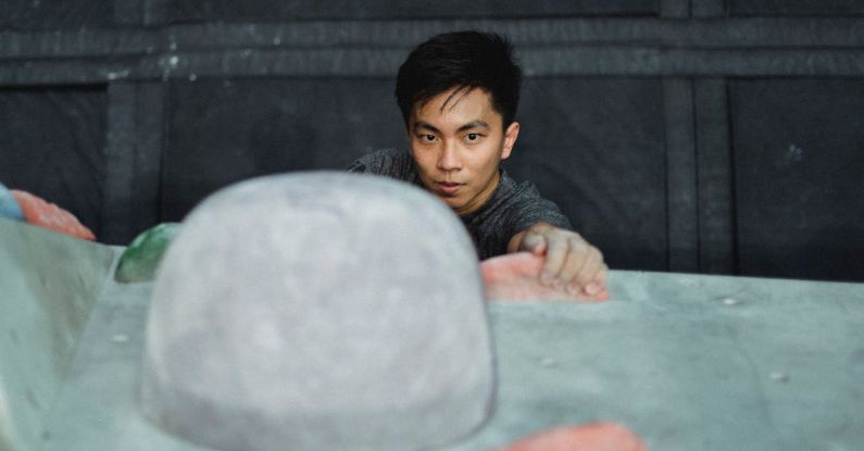 Fitness Goals - Focused Asian male athlete in gray sportive t-shirt climbing on climbing wall and looking forward